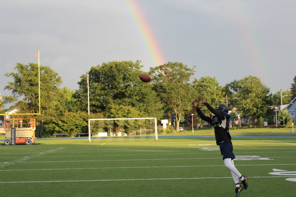 a man catching a football with a rainbow in the background